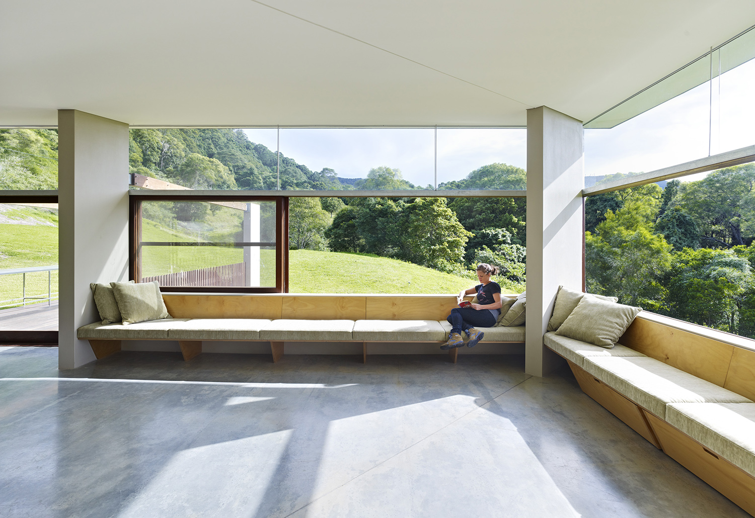 A woman reading on a window seat in the sunshine with sliding stacker windows open around her