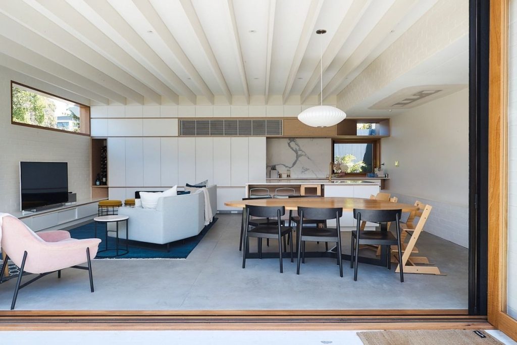View through open timber doors into an open plan living room & kitchen with custom windows in Blackbutt.