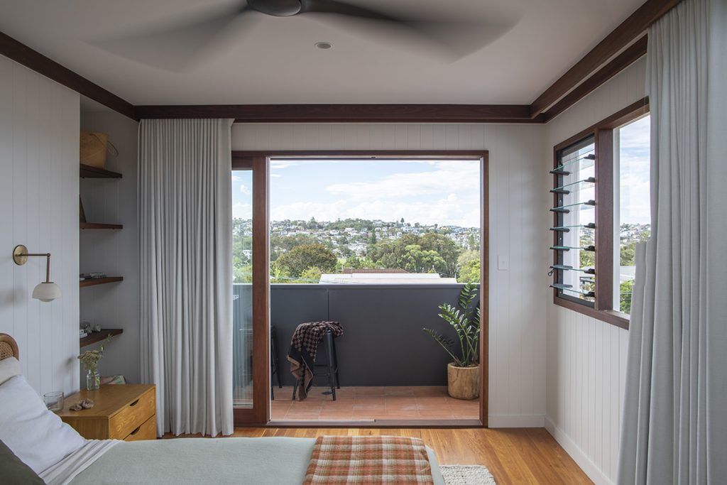 View from bedroom of a balcony and beyond framed by an open sliding door and a window unit with fixed and louvre panels.