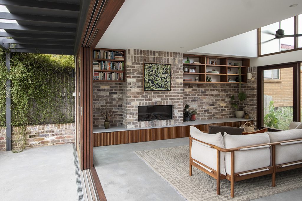 An open stacker sliding door in Spotted Gum separates the outdoor living area and modern lounge room with brick feature wall